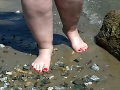 Fat bare legs with red pedicure walk along the bank of the sea, fetish.