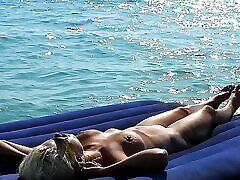 我在海滩上看着一个大胸脯的裸体女孩在床垫上晒日光浴。 慢动作